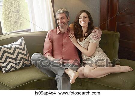 Picture - Portrait of smiling young couple on sitting room sofa. Fotosearch