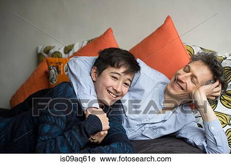 Stock Image - Portrait of teenage boy and father reclining on sofa. Fotosearch