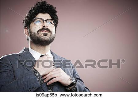 Stock Image - Portrait of young man adjusting tie. Fotosearch