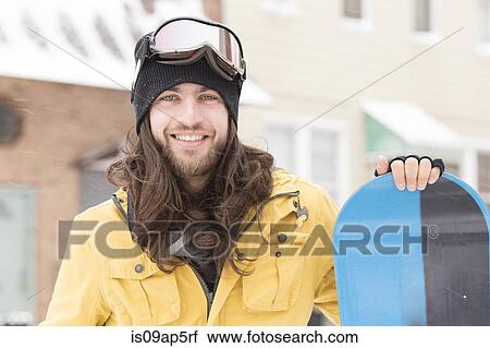 Stock Image - Portrait of young man holding snowboard on street. Fotosearch