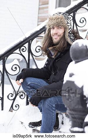 Stock Image - Portrait of young man sitting on snow covered front door steps. Fotosearch