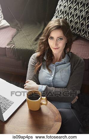Stock Photograph - Portrait of young woman drinking coffee and using laptop. Fotosearch
