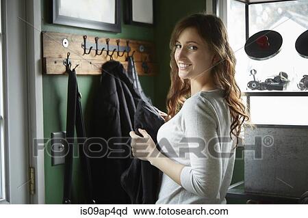 Stock Image - Portrait of young woman holding coat in cloakroom. Fotosearch