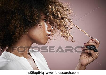 Stock Photography - Portrait of young woman pulling on strand of curly hair. Fotosearch
