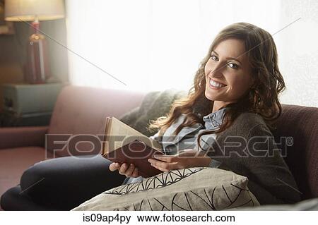 Stock Photo - Portrait of young woman reading book on living room sofa. Fotosearch