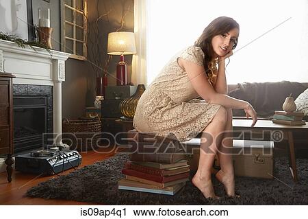 Portrait of young woman sitting on stack of books in living room View Large Photo Image Stock Image - Portrait of young woman sitting on stack of books in living room. Fotosearch