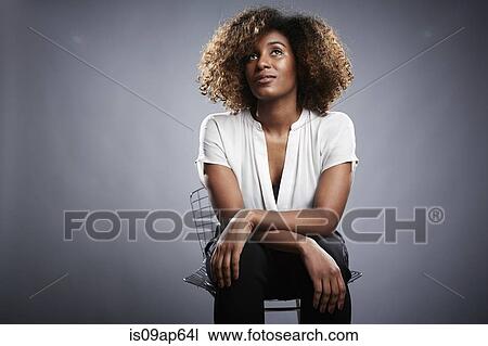 Stock Image - "Portrait of young woman sitting on chair, looking away". Fotosearch