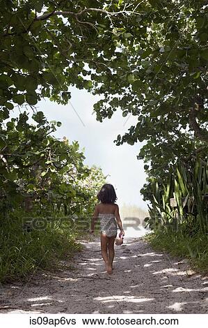 Stock Photograph - "Rear view of girl wearing bathing costume walking along woodland beach path, Anna Maria Island, Florida, USA". Fotosearch