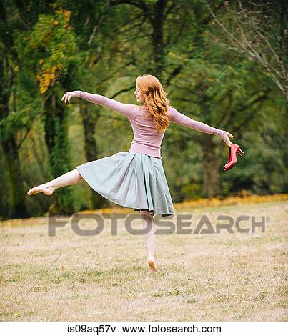 Stock Photo - Rear view of young female dancer poised holding red high heels in park. Fotosearch