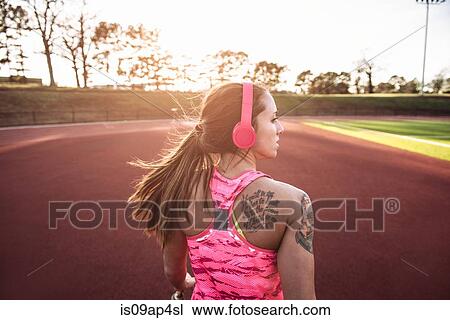 Stock Image - Rear view of young tattooed female athlete running on race track. Fotosearch