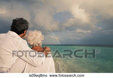 Picture - "Senior couple looking at rainbow over sea, Maldives". Fotosearch