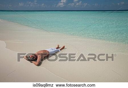 Stock Photo - "Senior man lying on snady beach, Maldives". Fotosearch