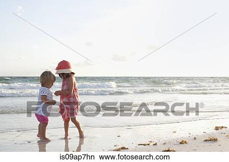 Picture - Siblings exploring on the beach at sunset. Fotosearch