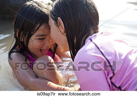 Stock Photography - Sisters playing in sea. Fotosearch