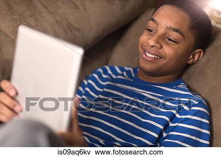 Smiling teenage boy reclining on sofa browsing digital tablet View Large Photo Image Stock Photo - Smiling teenage boy reclining on sofa browsing digital tablet. Fotosearch