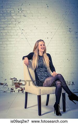 Studio portrait of a laughing young woman sitting in a chair View Large Photo Image Stock Photo - Studio portrait of a laughing young woman sitting in a chair. Fotosearch