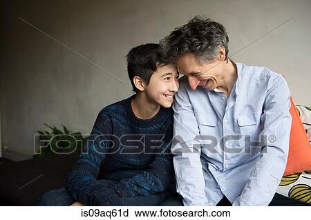 Stock Image - Teenage boy and father face to face on sofa. Fotosearch