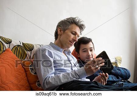 Teenage boy and father reading smartphone texts on sofa View Large Photo Image Stock Image - Teenage boy and father reading smartphone texts on sofa. Fotosearch
