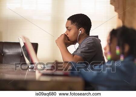 Stock Image - Teenage boy and sister at dining table using laptops. Fotosearch