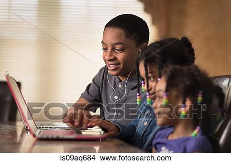 Picture - Teenage boy and sisters at dining table using laptop. Fotosearch