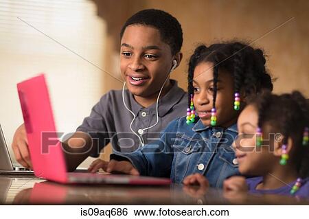 Teenage boy and sisters at dining table typing on laptop View Large Photo Image Stock Photograph - Teenage boy and sisters at dining table typing on laptop. Fotosearch