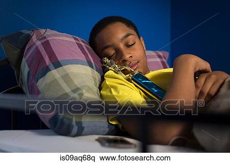 Stock Photography - Teenage boy asleep in bunkbed hugging trophy. Fotosearch