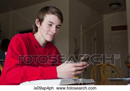 Stock Image - Teenage boy checking smartphone at dining room table. Fotosearch
