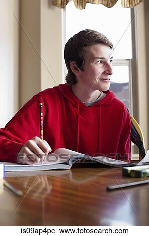 Stock Image - Teenage boy doing homework at dining room table. Fotosearch