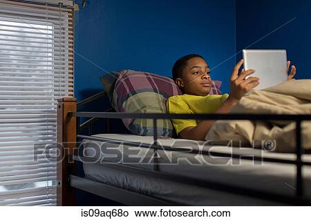 Picture - Teenage boy lying in bunkbed browsing digital tablet. Fotosearch