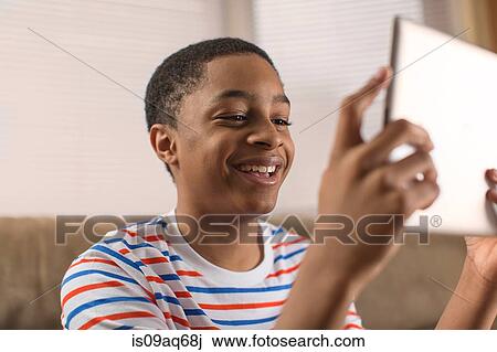Stock Image - Teenage boy posing for digital tablet selfie on sofa. Fotosearch