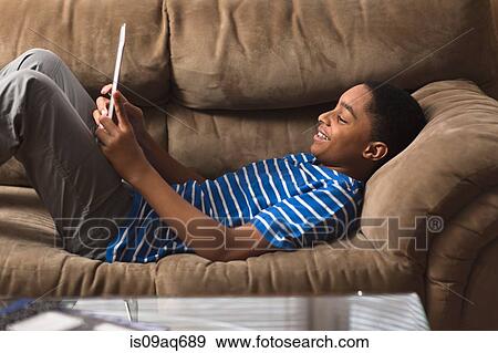Stock Photo - Teenage boy reclining on sofa browsing digital tablet. Fotosearch