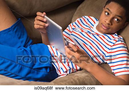 Stock Image - Teenage boy reclining on sofa with digital tablet. Fotosearch