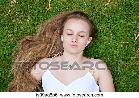"Teenage girl lying on grass, wearing earphones" View Large Photo Image Stock Photograph - "Teenage girl lying on grass, wearing earphones". Fotosearch