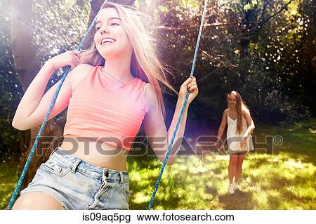 Teenage girl pushing her friend on tree swing View Large Photo Image Stock Image - Teenage girl pushing her friend on tree swing. Fotosearch
