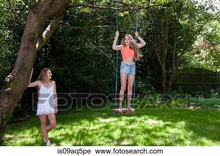 "Teenage girl swinging on tree swing, while friend watches on" View Large Photo Image Stock Image - "Teenage girl swinging on tree swing, while friend watches on". Fotosearch