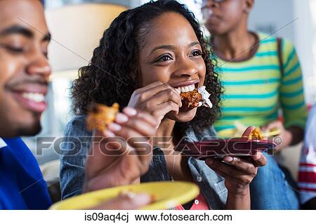Stock Image - Three adult friends eating takeaway on living room sofa. Fotosearch