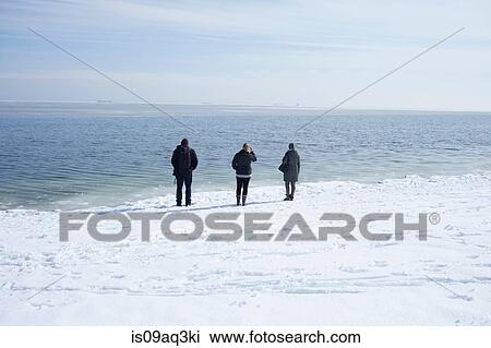 Stock Image - "Three adults looking out to sea, Fairfield, Connecticut, USA". Fotosearch
