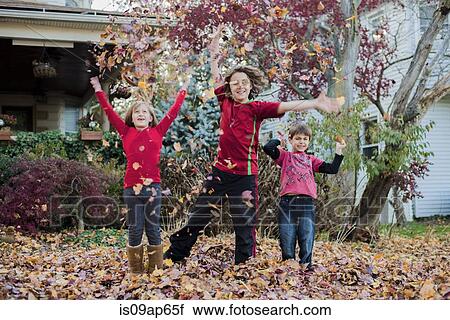 Stock Image - Three siblings playing with autumn leaves in garden. Fotosearch