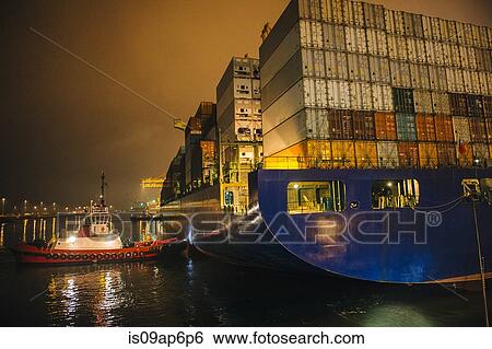 Stock Photograph - "Tugboat manoeuvring container ship on river at night, Tacoma, Washington, USA". Fotosearch