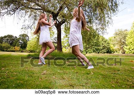 Stock Photo - "Two teenage girls dancing in field, low angle view". Fotosearch