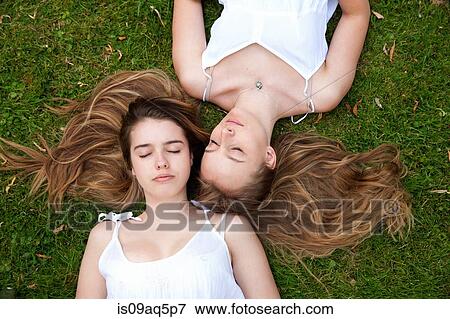Stock Photo - "Two teenage girls lying on grass, eyes closed". Fotosearch