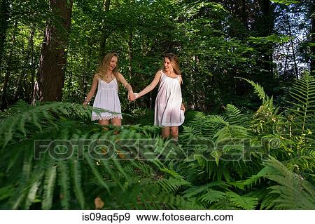 Stock Photo - "Two teenage girls walking through forest, hand in hand". Fotosearch