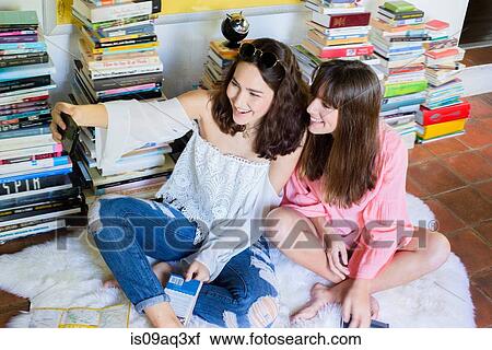 Stock Image - Two young female friends sitting on floor taking smartphone selfie. Fotosearch