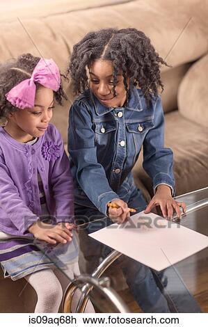 Stock Image - Two young sisters drawing on coffee table. Fotosearch