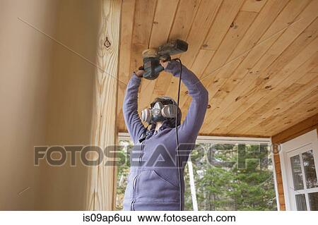 Stock Photograph - Woman sanding wooden ceiling in house. Fotosearch