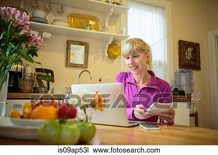 Woman working in kitchen table reading instruction booklet and using laptop View Large Photo Image Stock Image - Woman working in kitchen table reading instruction booklet and using laptop. Fotosearch