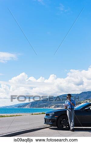 Young businessman at coast parking lot talking on smartphone whilst reading paperwork View Large Photo Image Stock Photograph - Young businessman at coast parking lot talking on smartphone whilst reading paperwork. Fotosearch