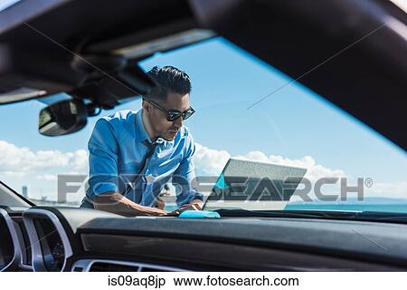 Young businessman at coast parking lot using laptop on car hood View Large Photo Image Stock Photography - Young businessman at coast parking lot using laptop on car hood. Fotosearch