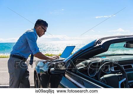 Young businessman at coast parking lot typing on laptop on car hood View Large Photo Image Stock Photography - Young businessman at coast parking lot typing on laptop on car hood. Fotosearch