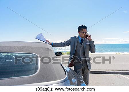 Young businessman at coastal parking lot talking on smartphone View Large Photo Image Stock Photo - Young businessman at coastal parking lot talking on smartphone. Fotosearch